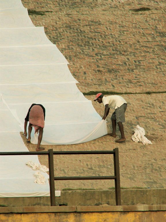 INDIA - VARANASI - twee mannen leggen lakens om te drogen bij de Ganges rivier