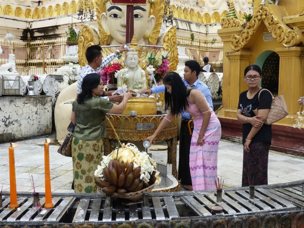 YANGON - enkele Myanmarezen gieten water over een boeddhabeeld op het complex van de Schwedagonpagode