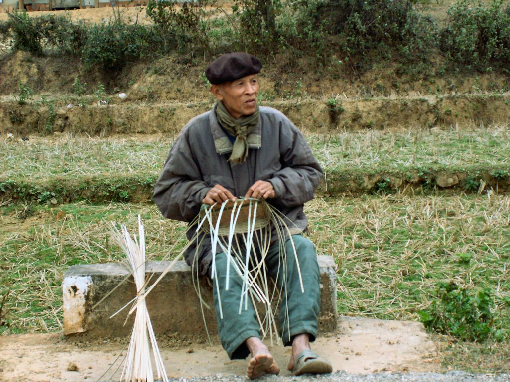 MAI CHAU - een oude man die een mand aan het maken is